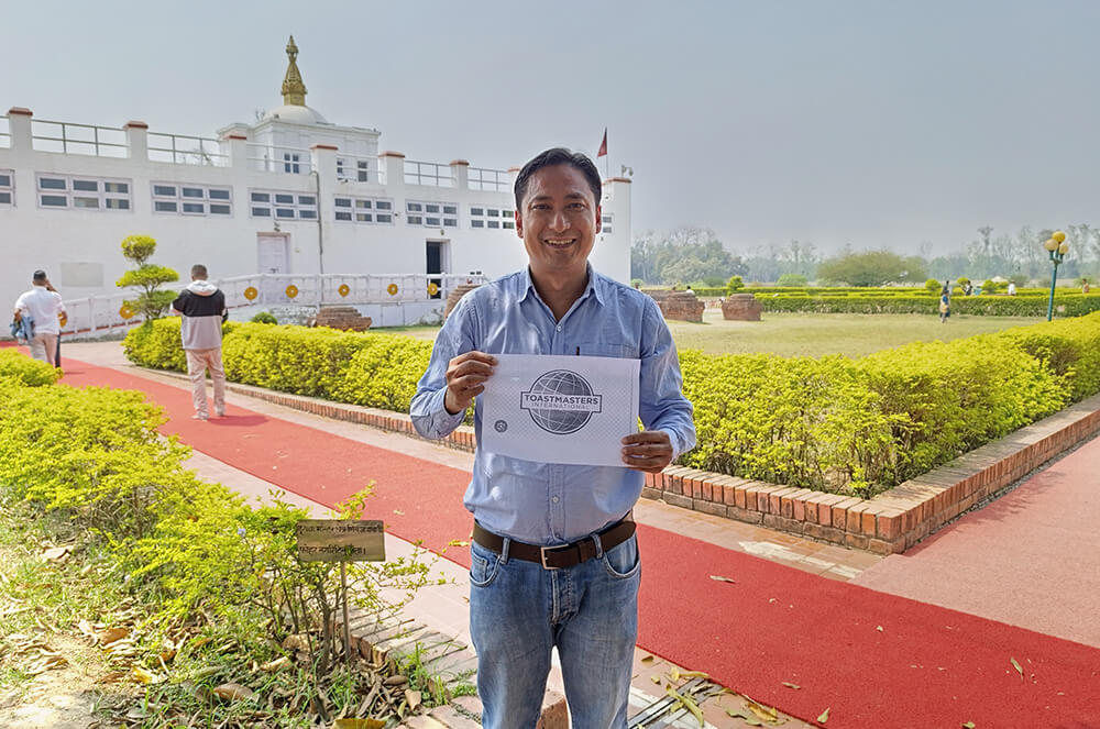 Man holding Toastmasters logo outdoors in front of Maya Devi Temple in Nepal