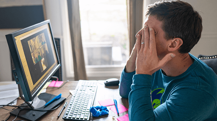 Man in front of computer with hands over eyes