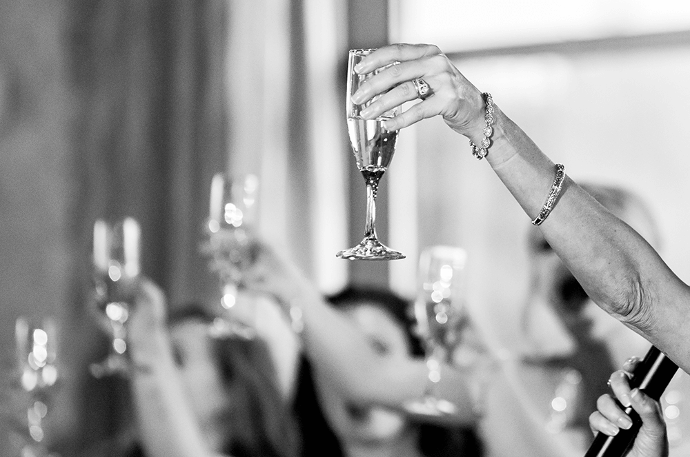 Several hands holding up glasses while toasting at a special occasion