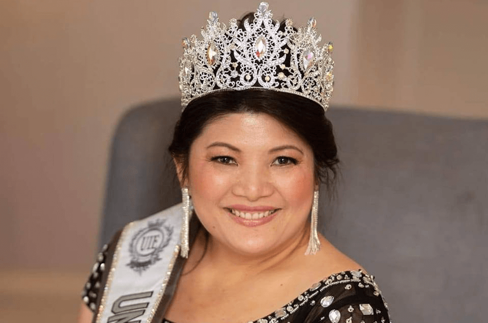 Woman in black dress smiling while wearing sash and crown